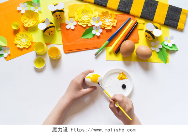 正在画画的学生孩子手女孩画一个复活节彩蛋。蛋一只黄蜜蜂。白色背景。创意材料,